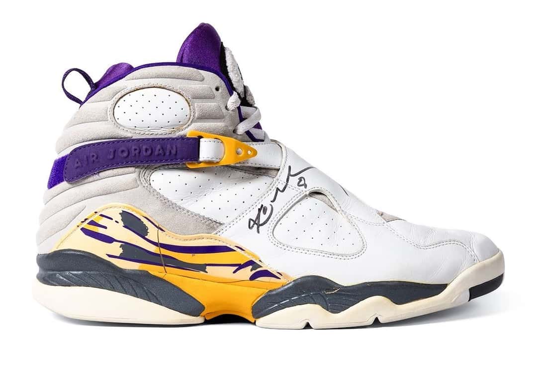 Air Jordan 8 de Kobe Bryant de perfil, blancas con las tiras cruzadas violetas, detalles amarillos en la suela y la firma de Kobe en el lateral