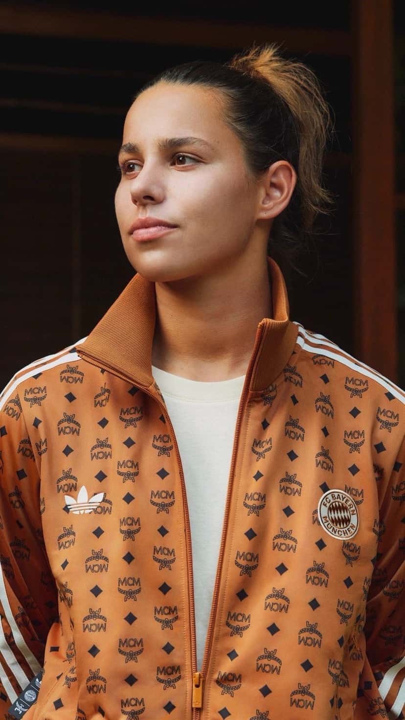 Mujer con la campera deportiva de la colección MCM x FC Bayern x adidas en coñac con el monograma y el escudo del club