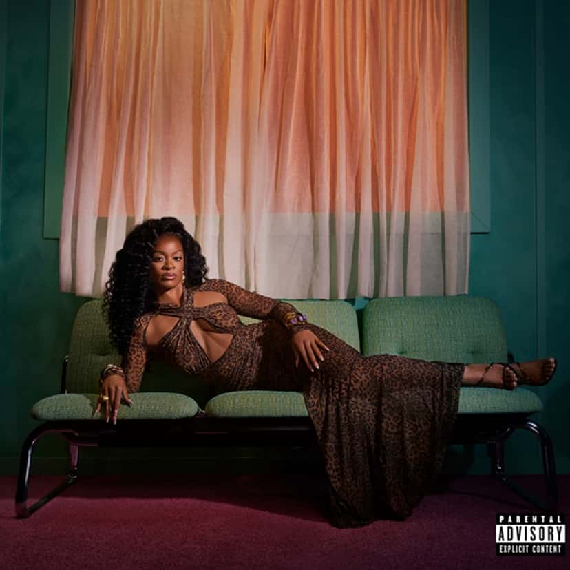 Portada de Vacancy, el disco original: Ari Lennox con vestido de animal print, recostada en un sillón verde frente a una ventana con cortinas rosadas, en una habitación de paredes verdes