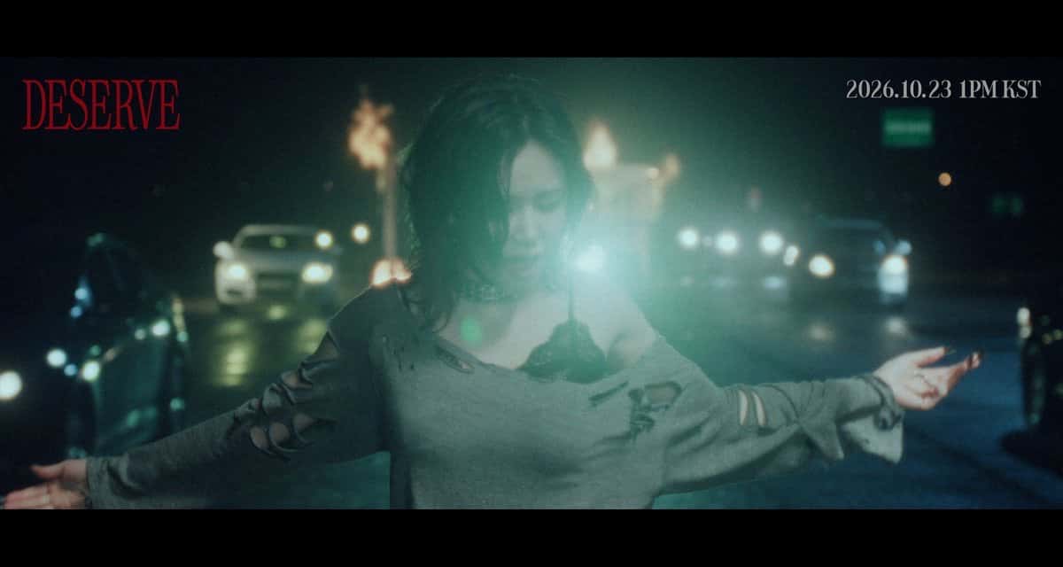Adelanto oficial del video de «DESERVE»: una integrante de BABYMONSTER, de noche en una calle con autos y luces encandilantes, con los brazos abiertos; arriba, el título DESERVE en rojo y la fecha 2026.10.23 1PM KST