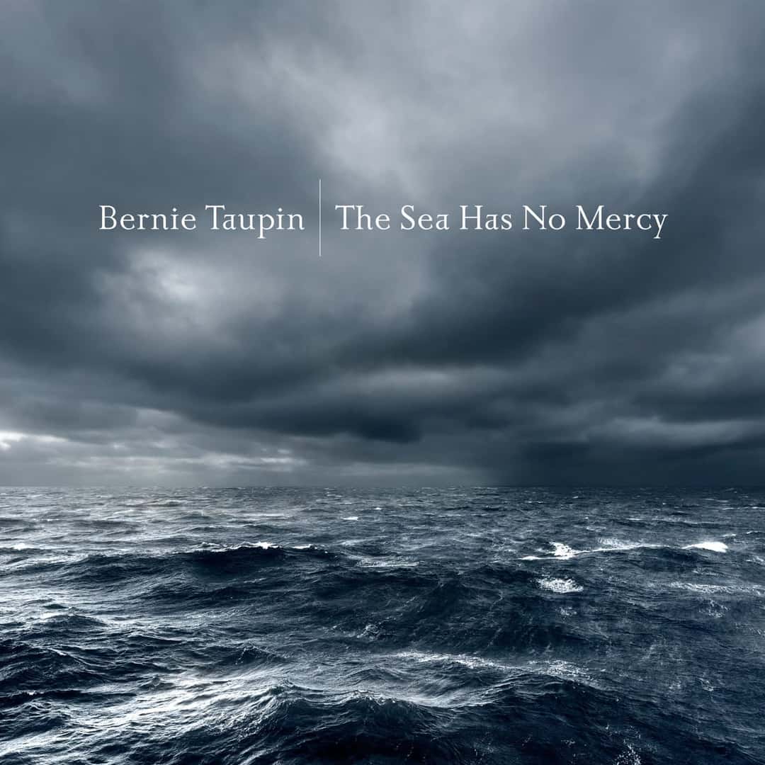 Portada de «The Sea Has No Mercy»: un mar oscuro y agitado bajo un cielo de nubes grises de tormenta, con el nombre de Bernie Taupin y el título en letras blancas