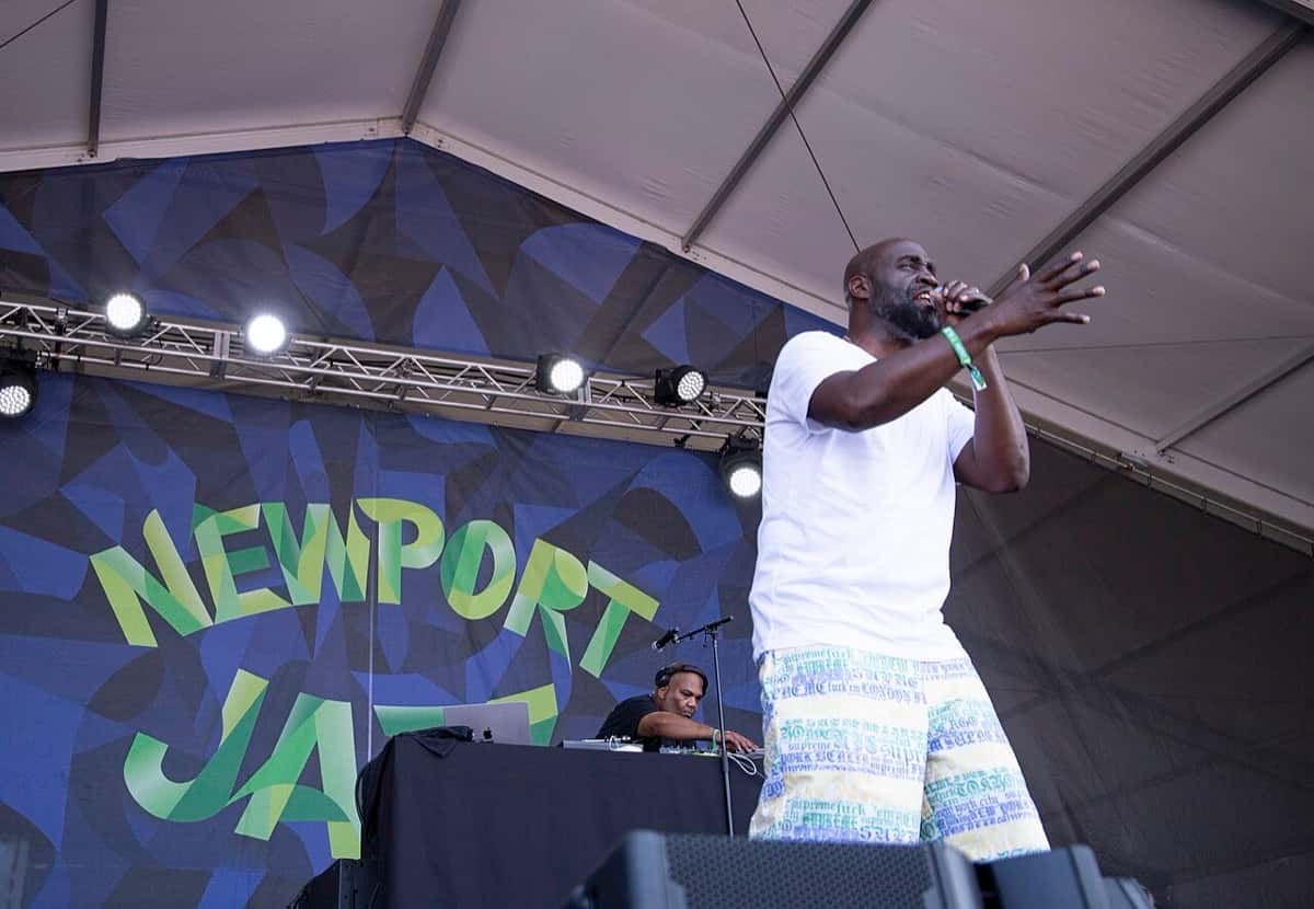 De La Soul en vivo en el Newport Jazz Festival de 2025 (foto de archivo): un integrante de remera blanca rapea con el micrófono y el brazo en alto, con el cartel del festival detrás