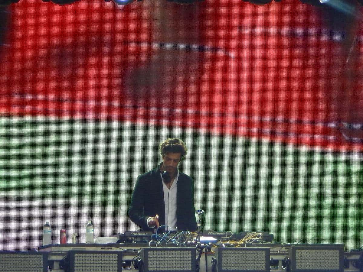Gesaffelstein, de saco negro y camisa blanca, pasa música detrás de una consola de DJ frente a una pantalla gigante con imágenes rojas, en agosto de 2014 (foto de archivo)