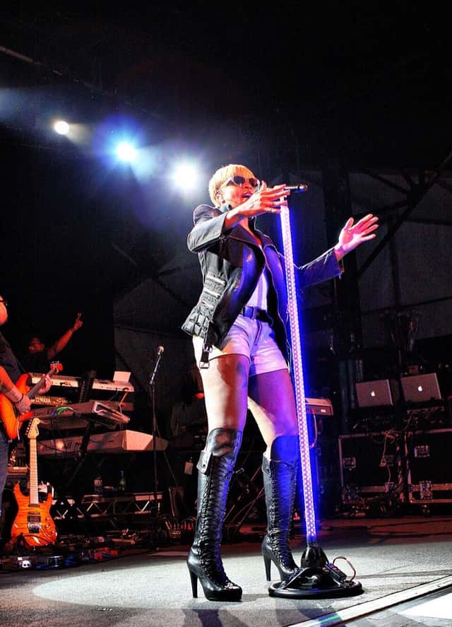Mary J. Blige canta en vivo con anteojos de sol, campera negra, short plateado y botas altas, junto a un pie de micrófono iluminado, en el festival Raggamuffin de 2011 (foto de archivo). Foto: Eva Rinaldi, CC BY-SA 2.0, vía Wikimedia Commons