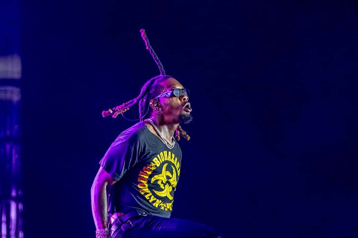 Foto de archivo de Offset en el escenario del Clout Festival 2024, con anteojos oscuros, trenzas en el aire y una remera negra con estampa amarilla, bajo luces violetas