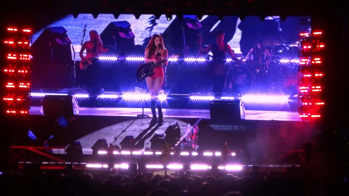 Olivia Rodrigo canta con una guitarra eléctrica en el escenario de Lollapalooza Argentina, rodeada de su banda y de luces violetas y rojas (foto de archivo, marzo de 2025)