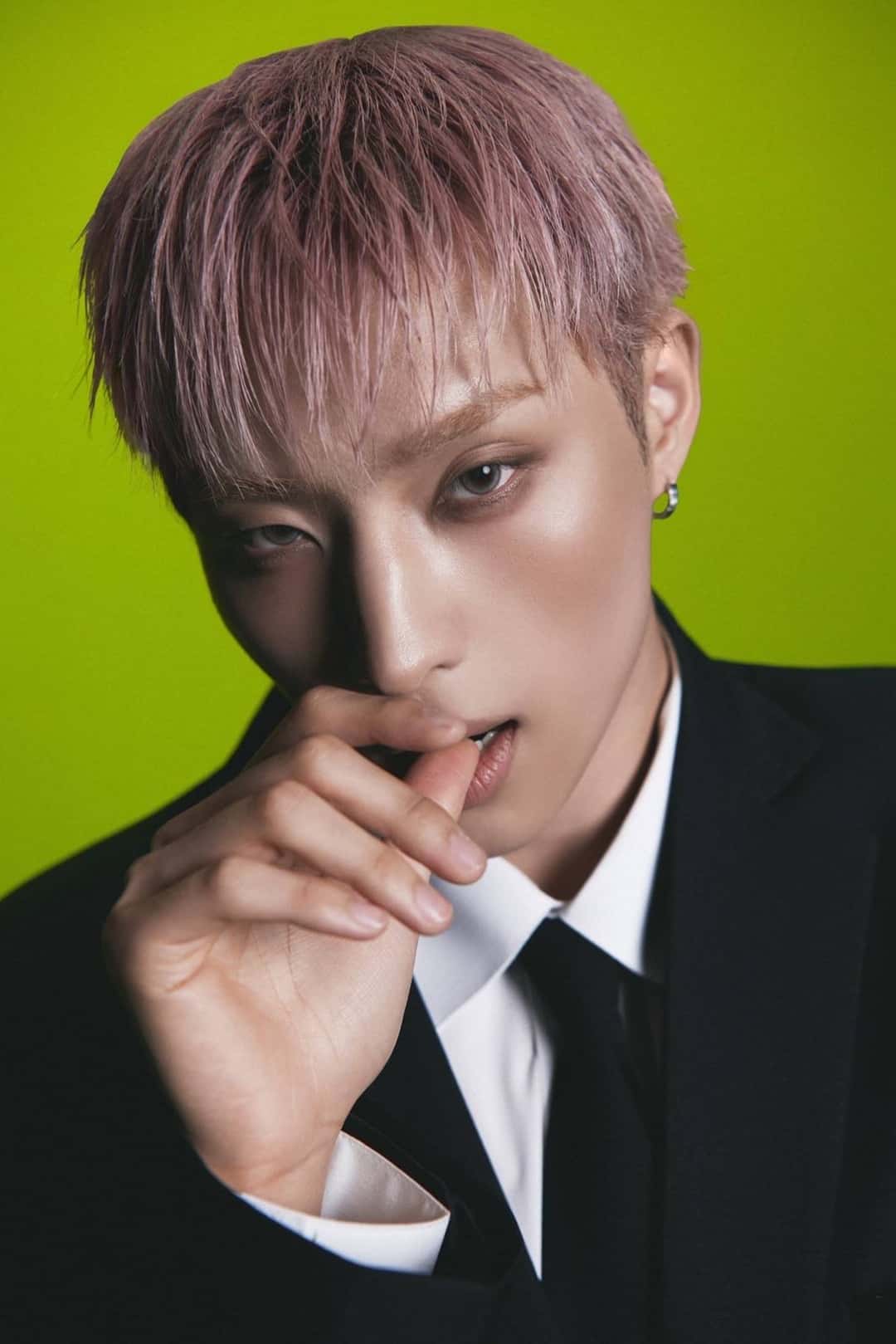 Foto conceptual individual oficial de Keeho para «BLOW UP»: el cantante, con pelo rosado, traje negro y corbata, con la mano cerca de la boca, frente a un fondo verde