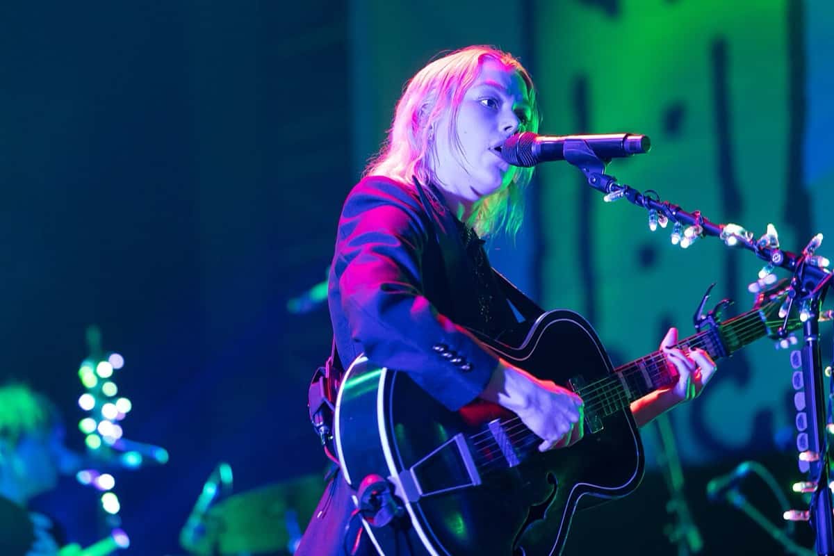 Phoebe Bridgers canta y toca una guitarra negra, con saco oscuro y pelo rubio, bajo luces violetas y verdes, en el festival Laneway de Sídney en 2023 (foto de archivo)