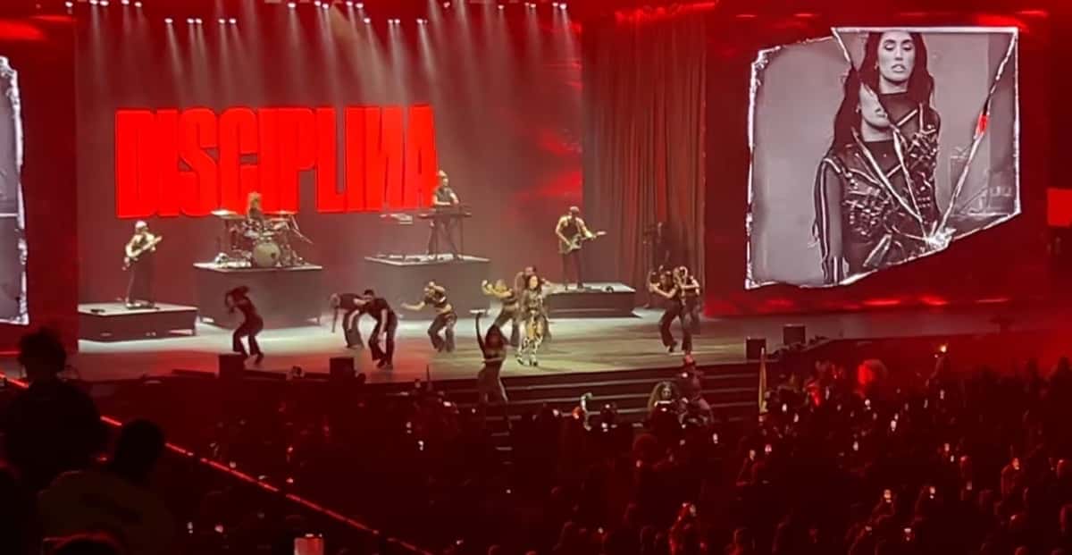 Foto de archivo de Lali en el escenario de los Premios Gardel 2024: la cantante baila con su cuerpo de baile bajo luces rojas, con la banda atrás, la palabra DISCIPLINA en letras rojas gigantes en la pantalla y su cara en blanco y negro en otra pantalla a la derecha. Foto: GabiAcop, Wikimedia Commons, CC BY 3.0