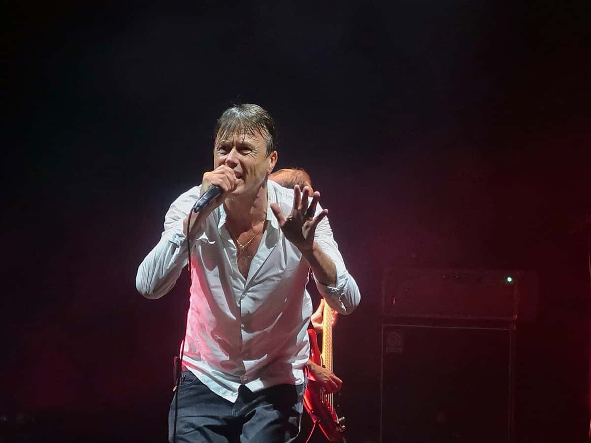 Brett Anderson, cantante de Suede, canta con camisa blanca abierta y el micrófono en la mano, con la otra mano levantada, sobre un escenario oscuro con luz roja, en el Royal Festival Hall de Londres en 2025 (foto de archivo)