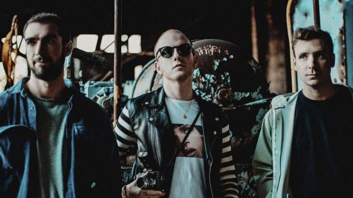 Foto de prensa de Two Door Cinema Club (foto de archivo): los tres integrantes posan entre maquinaria oxidada, uno con anteojos de sol y una cámara colgada