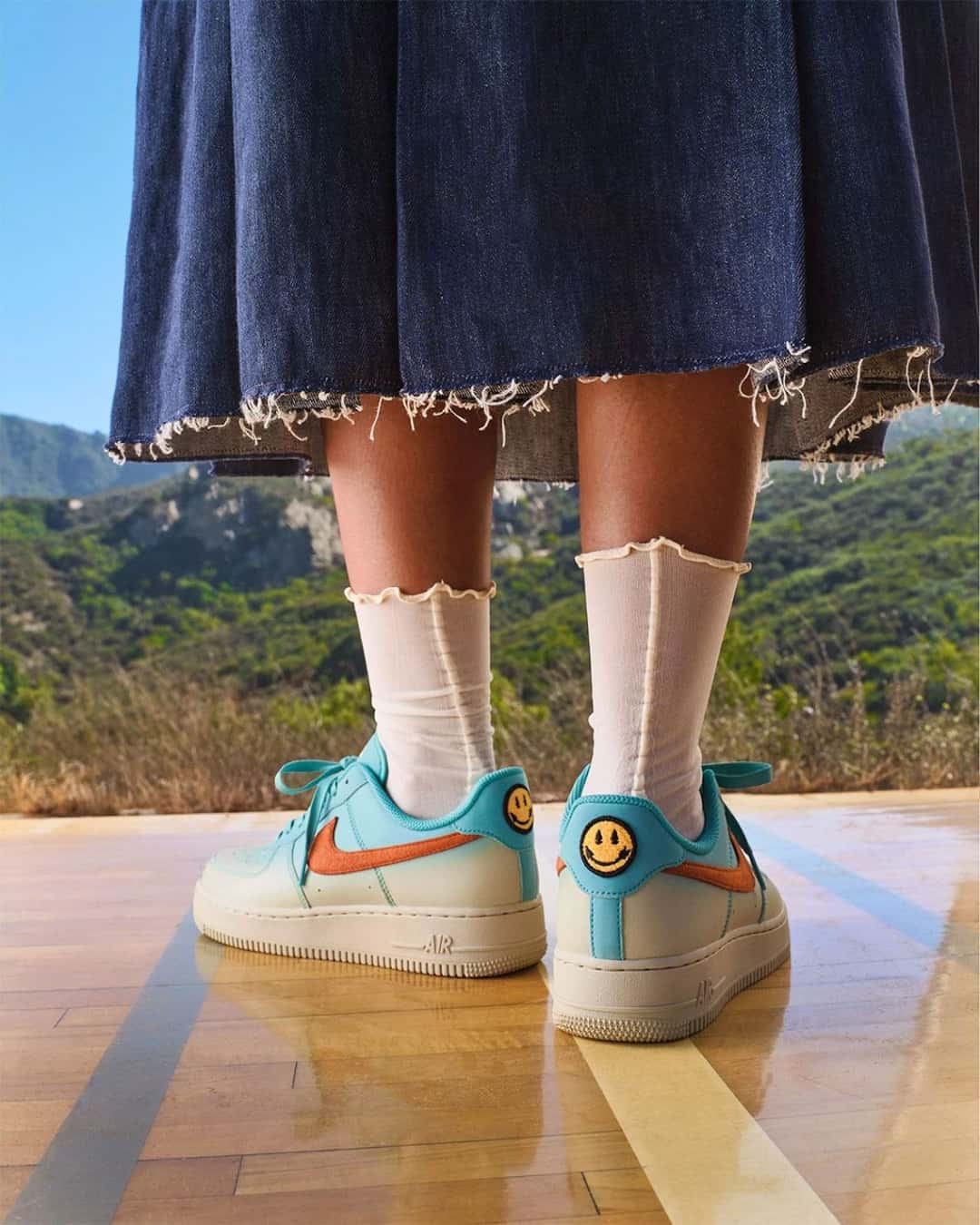 Nike Air Force 1 N7 puesto, con degradé beige y turquesa, Swoosh naranja y una carita sonriente en el talón