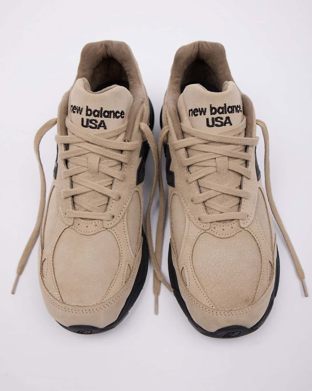 Par del JJJJound x New Balance 990v3 Tan Suede de frente, con cordones tan, lengüetas con la leyenda new balance USA bordada en negro y suela negra