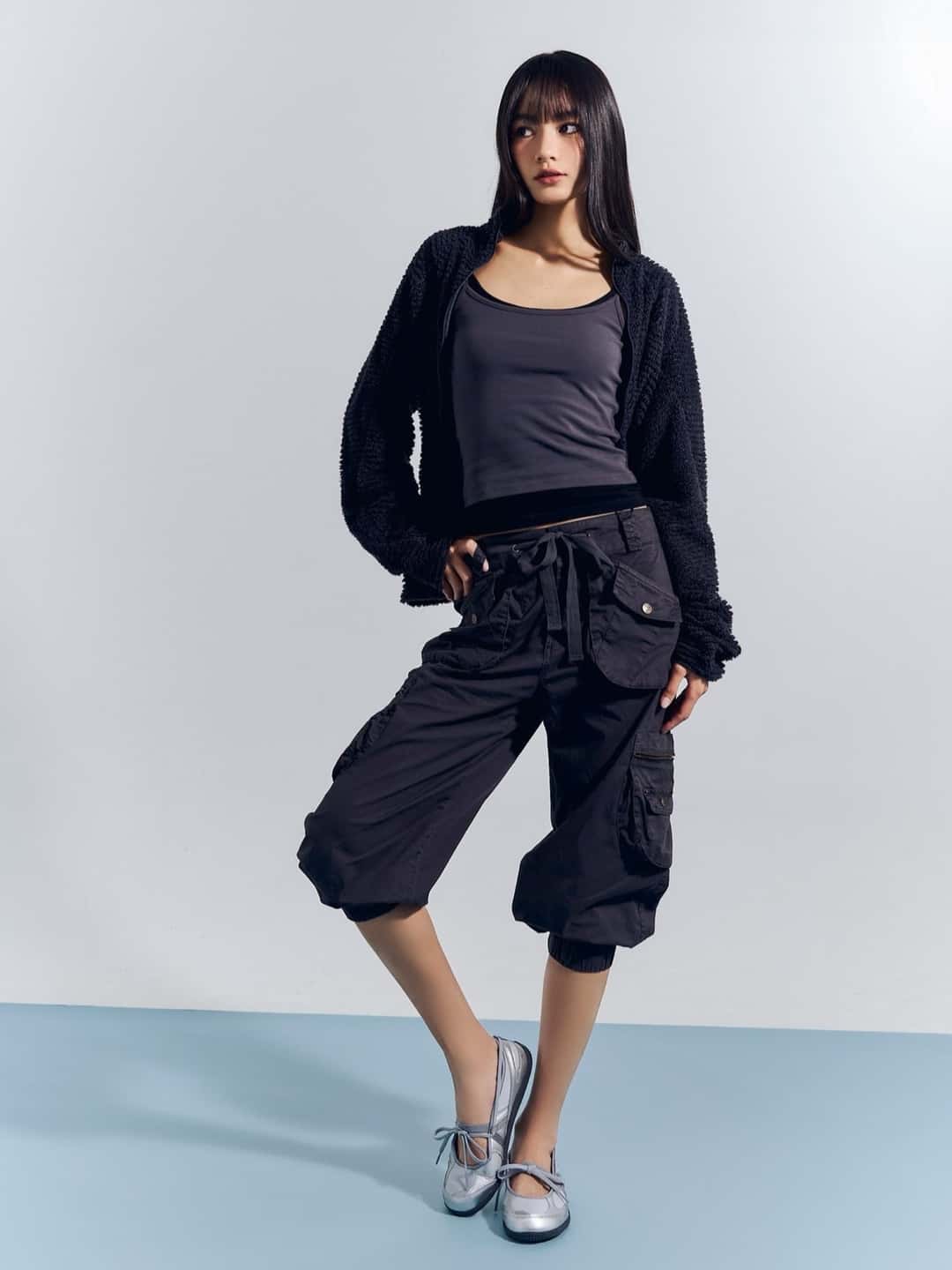 Modelo con campera y bermuda negras y un par de New Balance Flat Breeze plateadas, sobre fondo celeste