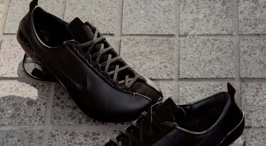 Par de Nike Ovolo 2.0 negras sobre baldosas de piedra, con la capellada de cuero liso, los cordones negros y el taco brillante