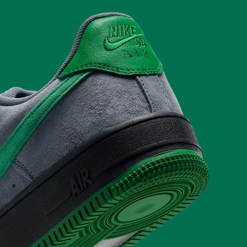 Talón del Nike SB Air Force 1 Low de Nocturnal en primer plano, con la pestaña de cuero verde con el logo Nike SB Air grabado, la gamuza gris, la mediasuela negra con Air grabado y la suela verde