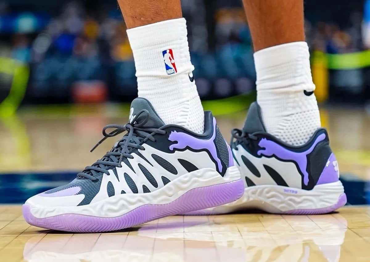 PUMA Hali 1 Teddy Lockart puestas en una cancha de básquet, con medias blancas de la NBA, cage blanco ondulado sobre base negra y gris oscura, felino de PUMA violeta y suela violeta