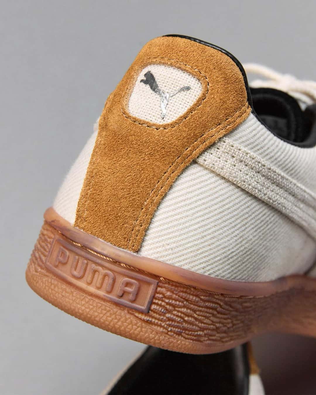 Vista trasera del PUMA x MASU Curio Suede, con la pieza del talón en gamuza marrón y el felino de PUMA en un recuadro de lona, el cuerpo marfil y la suela de goma color caramelo con el logo PUMA en relieve