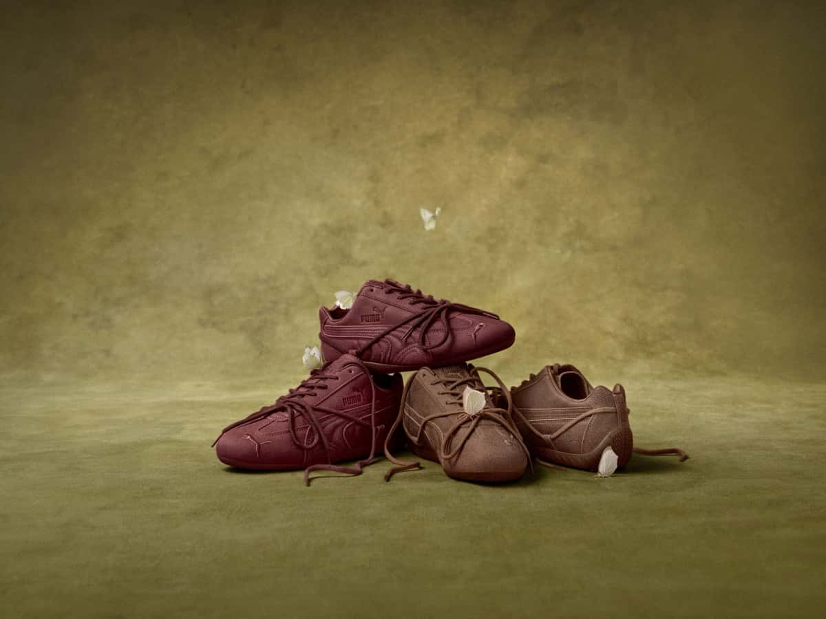 Cuatro zapatillas PUMA x ROSÉ Speedcat VTG, dos en bordó y dos en marrón, apiladas sobre un fondo verde oliva con mariposas blancas alrededor