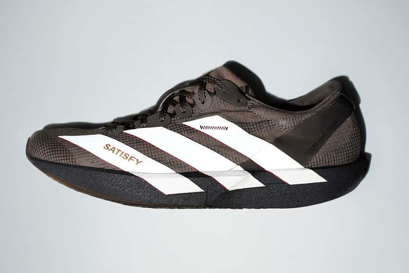 Adizero Adios Satisfy marrón de perfil, con las tres tiras blancas, la palabra SATISFY dorada en el antepié y la suela negra