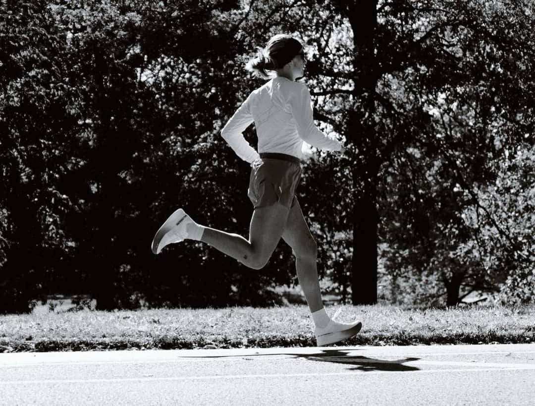 Una persona vestida de blanco corre en plena zancada sobre un camino de parque, en blanco y negro. Foto: Sébastien Lorsbach y Julien Caldarone para Salomon