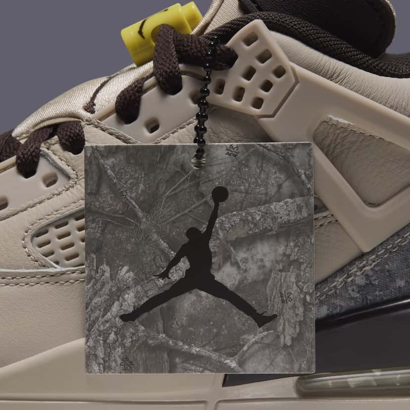 Primer plano del costado del Jordan Spizike Low Realtree Camo con un colgante cuadrado de camuflaje gris y Jumpman negro sujeto a los cordones marrones, junto a las alas crema y la traba de cordones amarilla