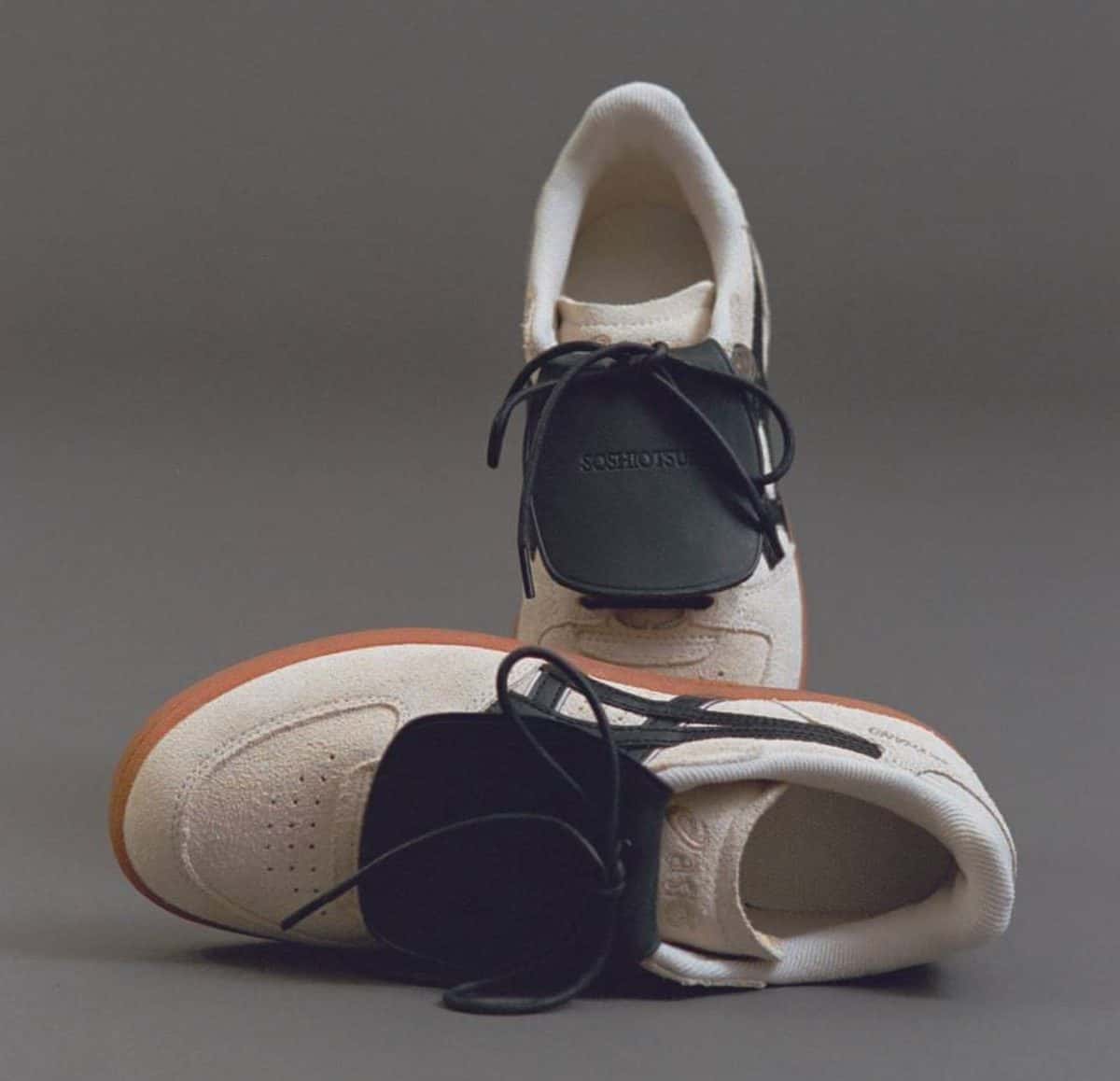 Par de la SOSHIOTSUKI x ASICS Skyhand OG en gamuza crema con las rayas ASICS negras, la suela de goma marrón y la lengüeta grande de cuero negro sobre los cordones