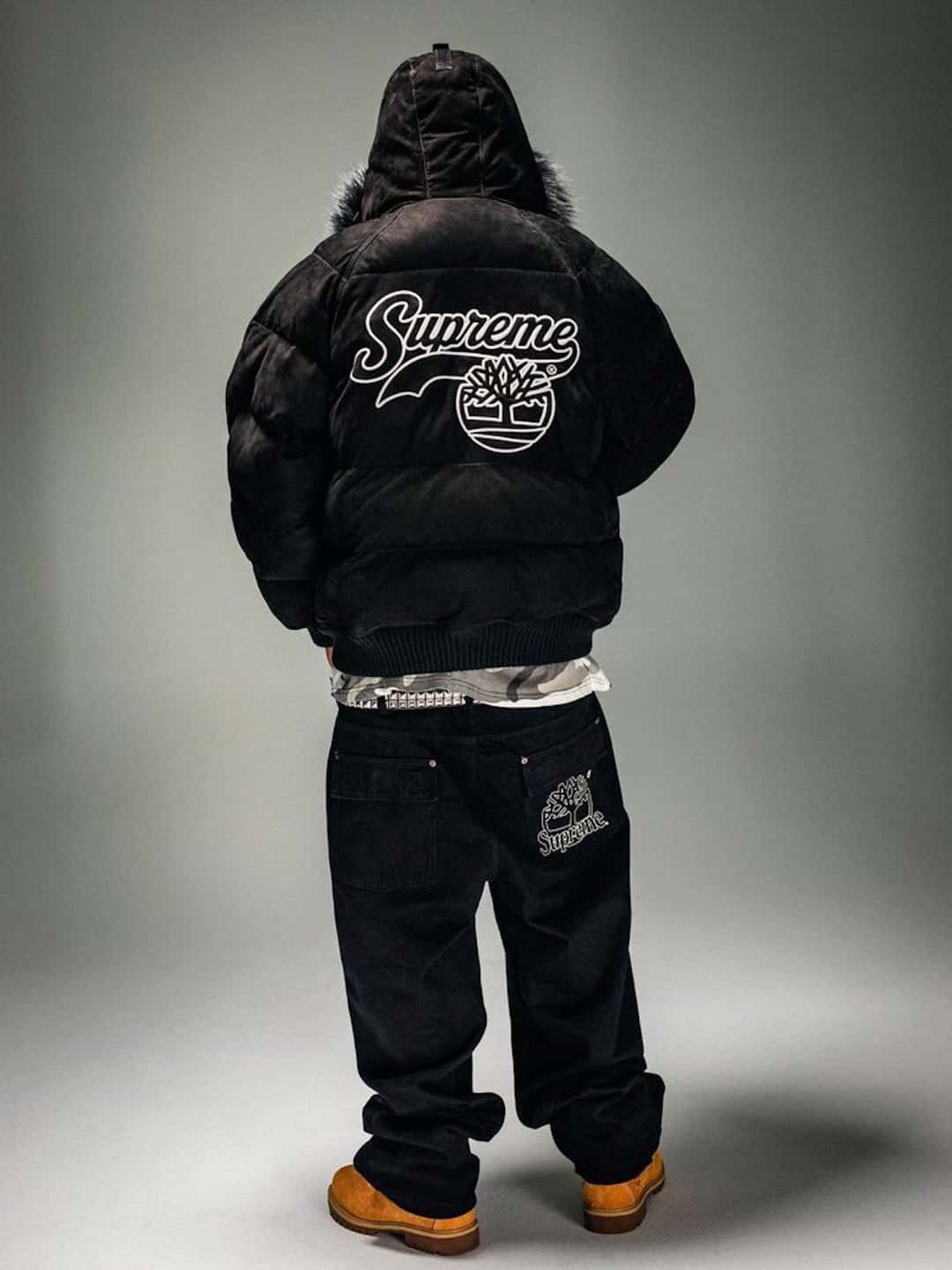 Modelo de espaldas con la campera Supreme x Timberland Suede Puffer negra, con el logo de Supreme y el árbol de Timberland en la espalda