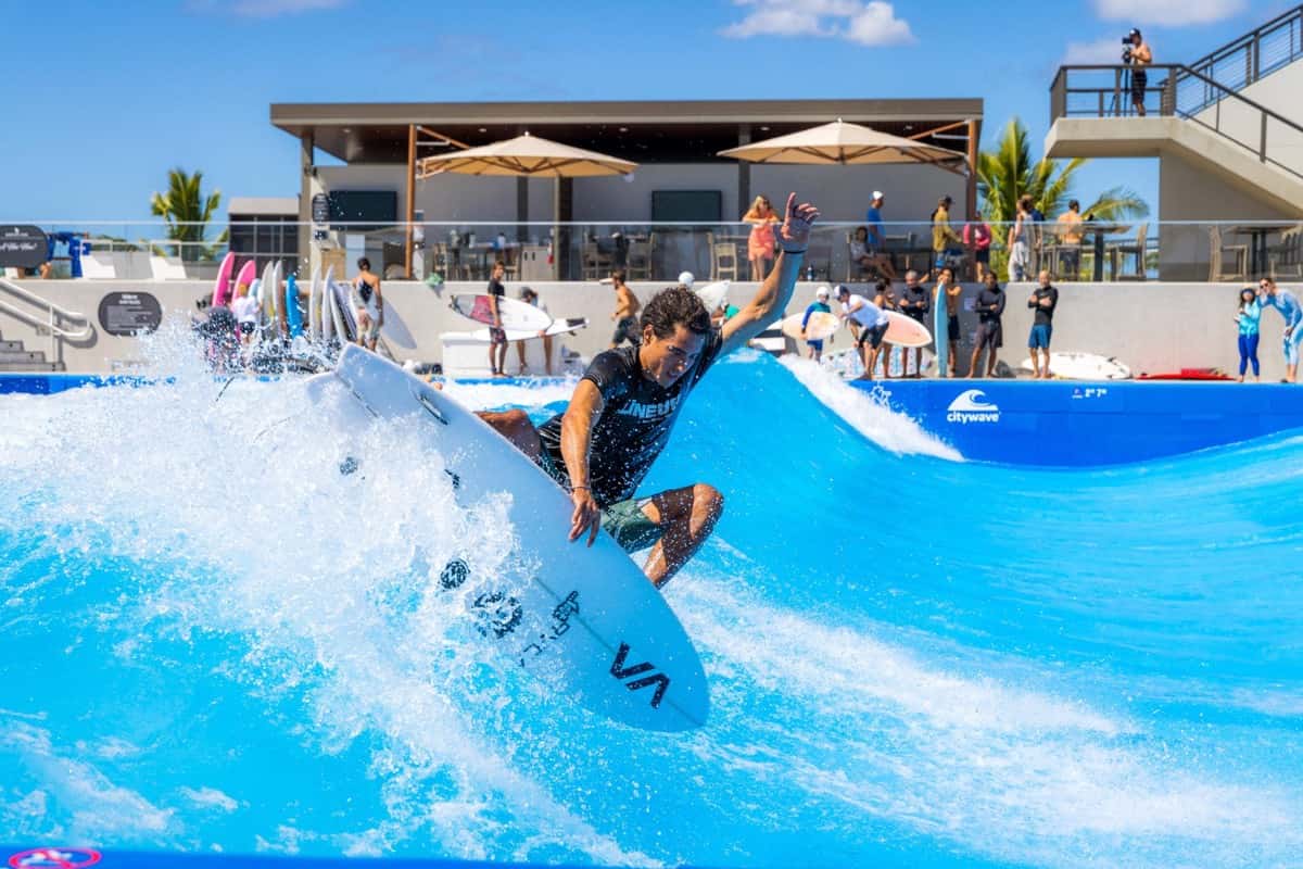 Un surfista hace un giro con la tabla de canto sobre la ola artificial de Wai Kai, en Oahu, con público en las gradas detrás