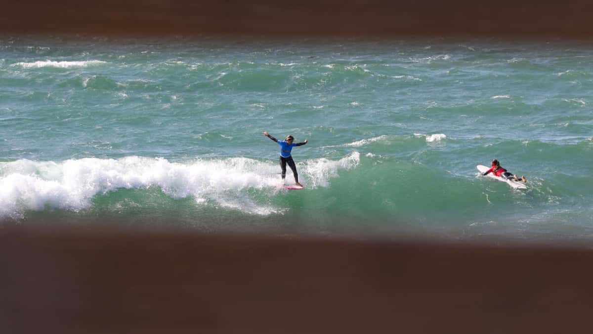 Story Martinez, con lycra azul, abre los brazos parada sobre su longboard en la espuma de una ola de Pismo Beach