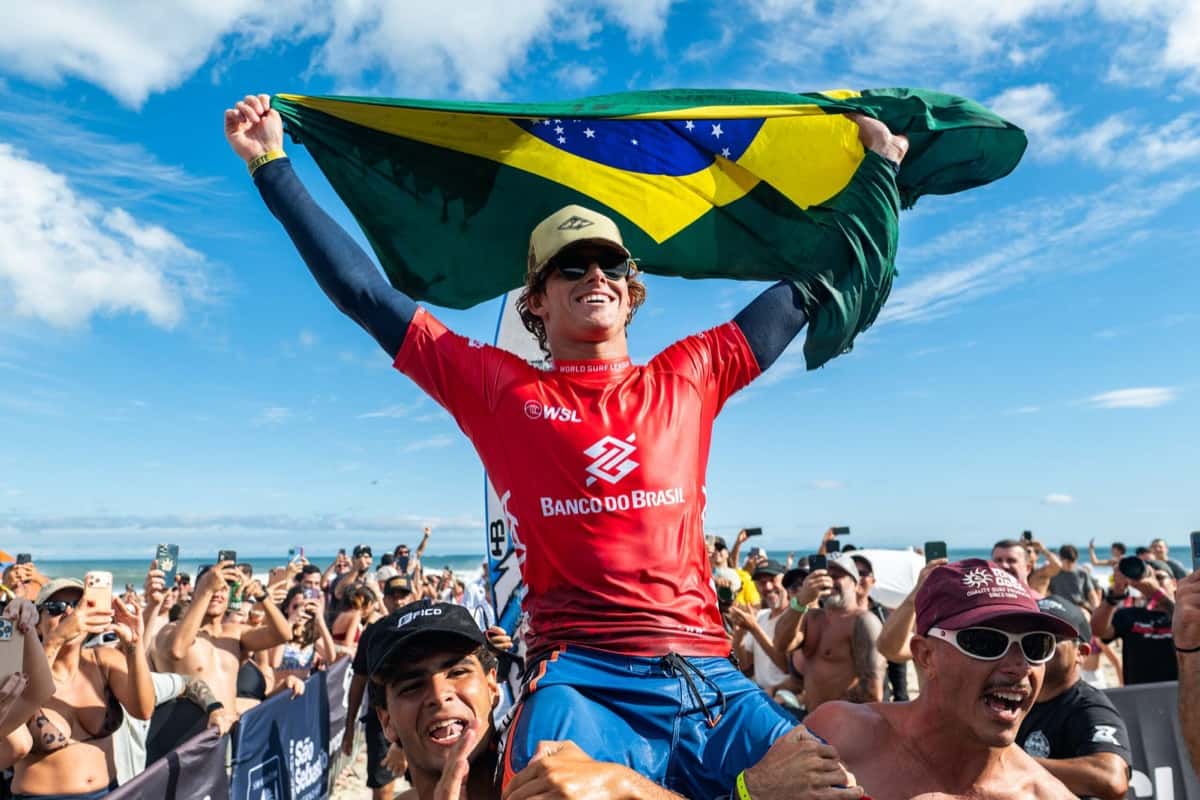 Ryan Kainalo, con la lycra roja de Banco do Brasil, levanta la bandera de Brasil en andas de la gente en la playa de Maresias