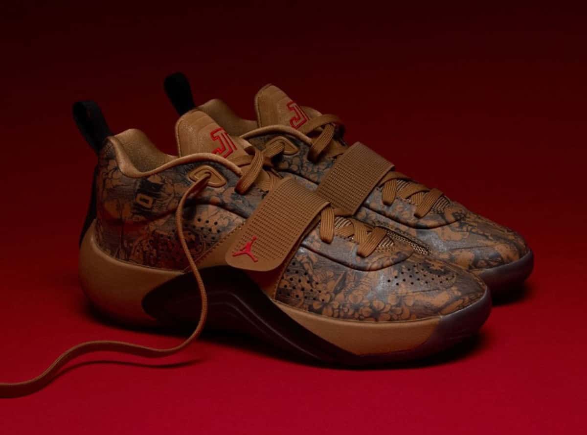 Par del Jordan Tatum 5 Laser sobre fondo rojo, con upper marrón tostado cubierto de gráficos grabados con flores, strap en el medio pie con Jumpman rojo y logo JT rojo en la lengüeta