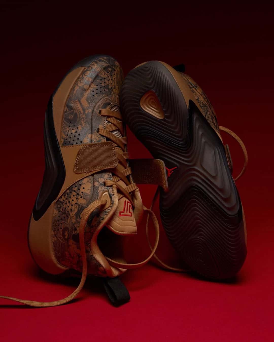 Par del Jordan Tatum 5 Laser parado sobre las puntas, uno de lado con los grabados y el strap, y el otro mostrando la suela marrón oscura con el dibujo de tracción y un Jumpman rojo